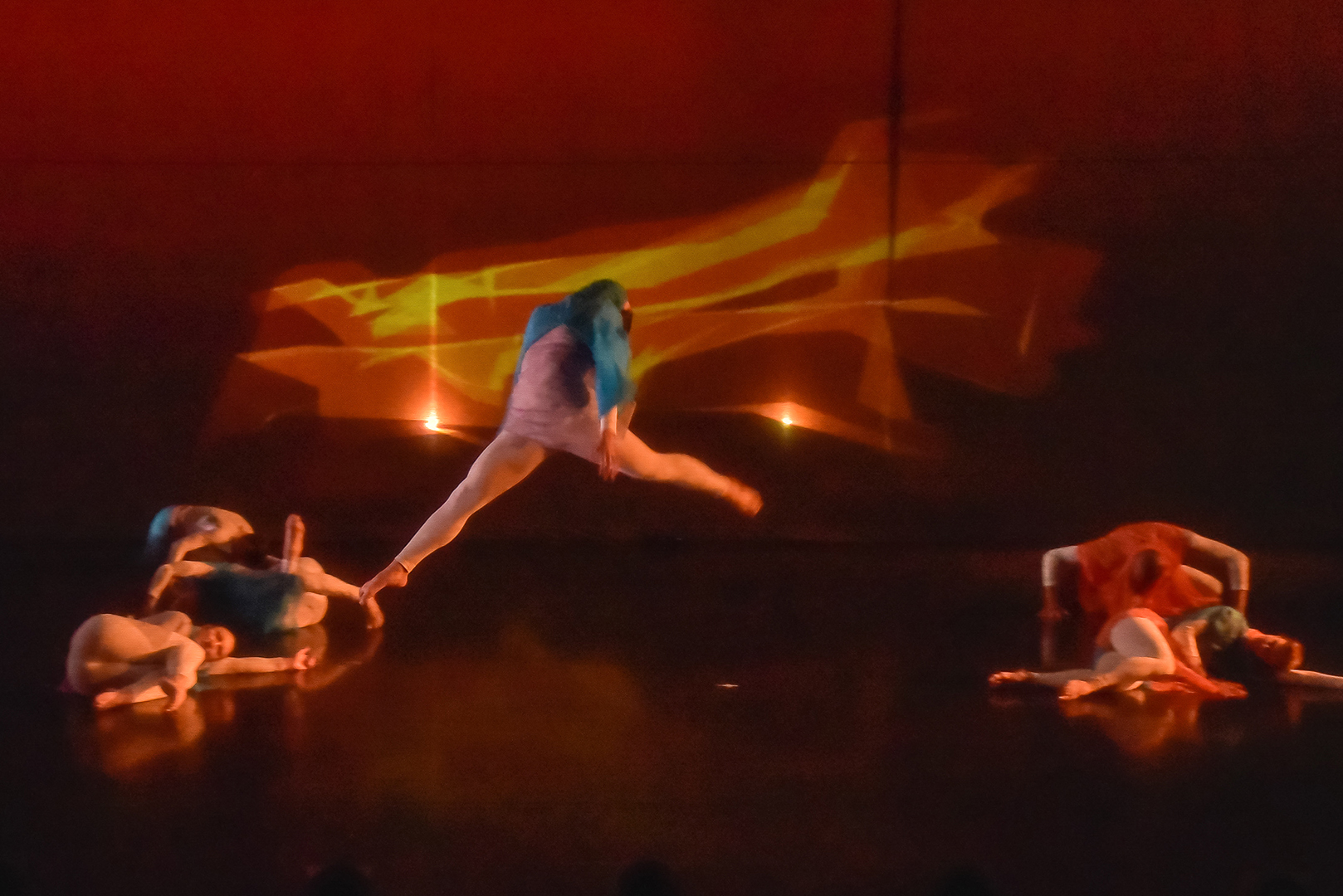 ESDC dancer leaping above fellow dancers in front of fiery polygonal trails during Kaatsbaan residency.
